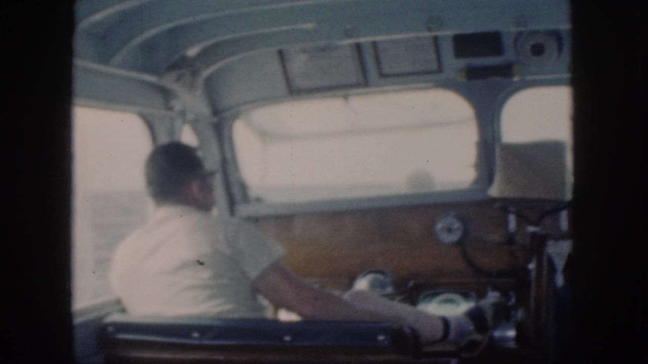 Man at the helm seen from behind inside a small boat cabin.