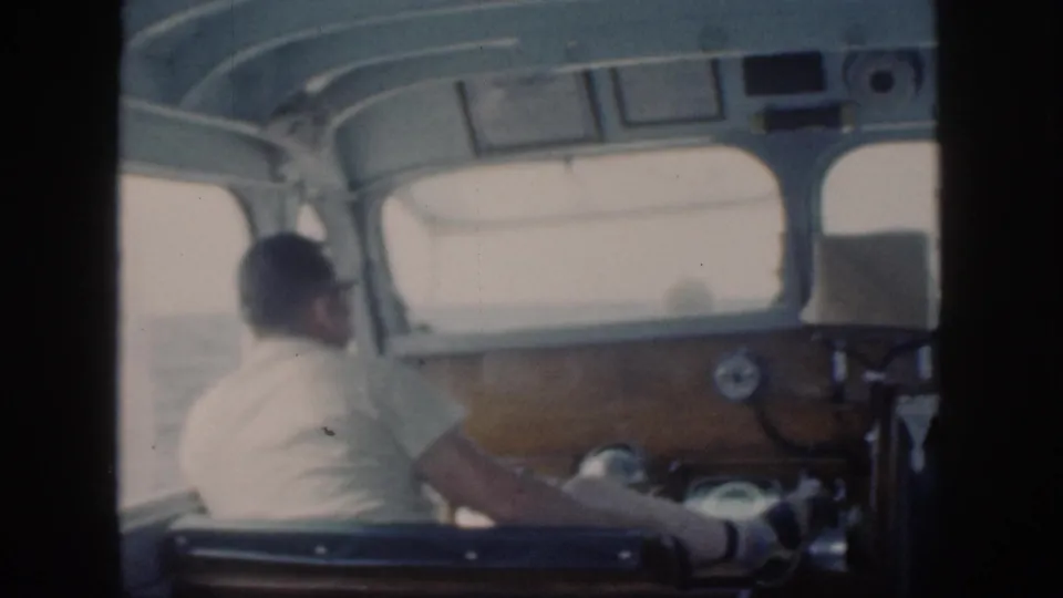 The man remains seated at the boat controls, viewed from behind in soft 8mm footage from Oahu, Hawaii.