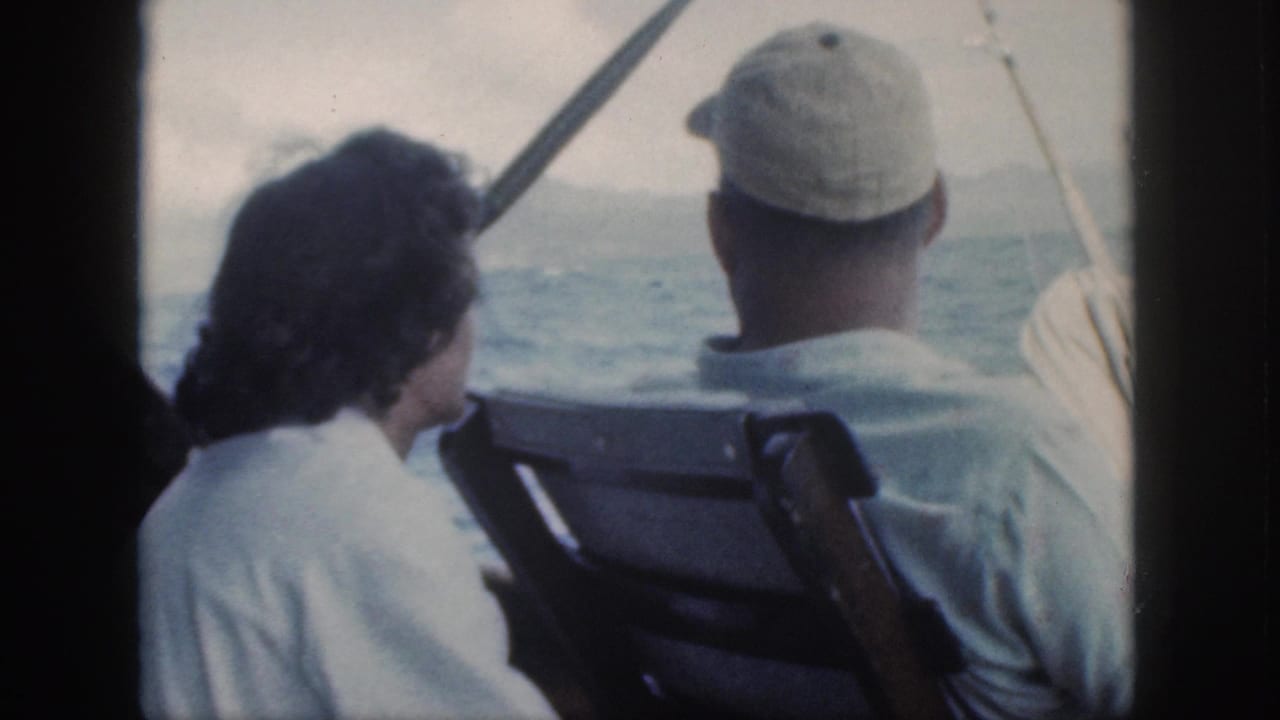 1959 Oahu home-movie frame showing two adults seated on a boat, seen from behind as they look toward the water.