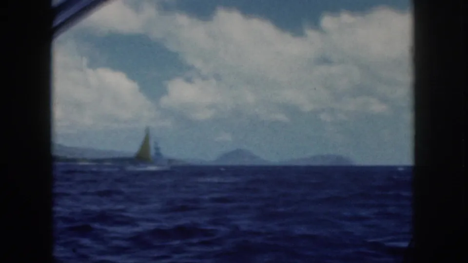 1959 Oahu ocean view with a small sailboat on the horizon, distant hills, and a cloudy sky in faded 8mm color.