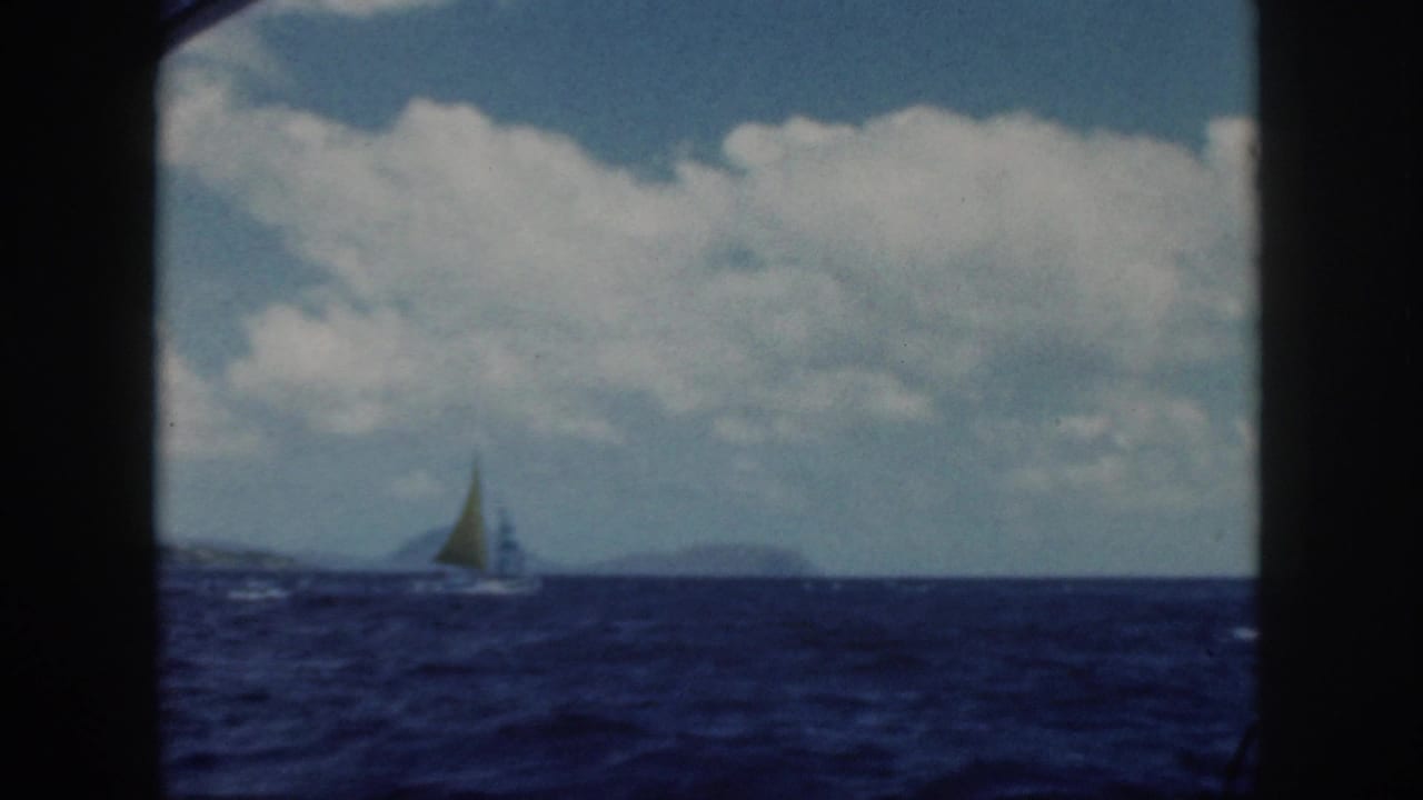 Small sailboat near the horizon on a choppy blue ocean beneath large white clouds.