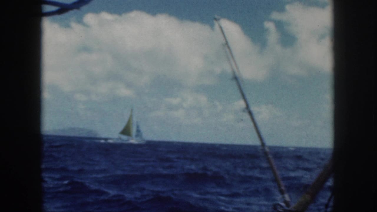1959 Oahu boat view of a distant sailboat with a green sail crossing blue water under a cloudy sky.
