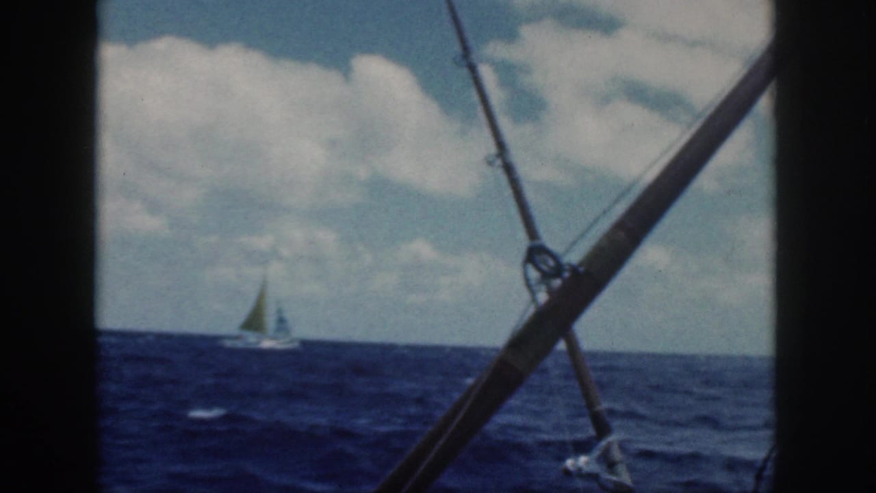 A small sailboat sits on the horizon off Oahu, framed by fishing rods and boat rigging in 8mm footage.