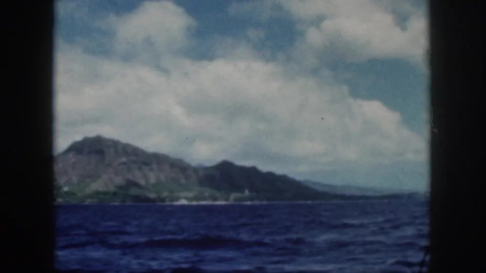 1959 8mm view from a boat toward Oahu's volcanic mountains and shoreline across deep blue ocean.