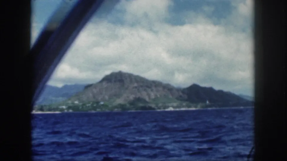1959 Oahu shoreline and volcanic ridge seen from a moving boat, with a curved dark window edge crossing the frame.