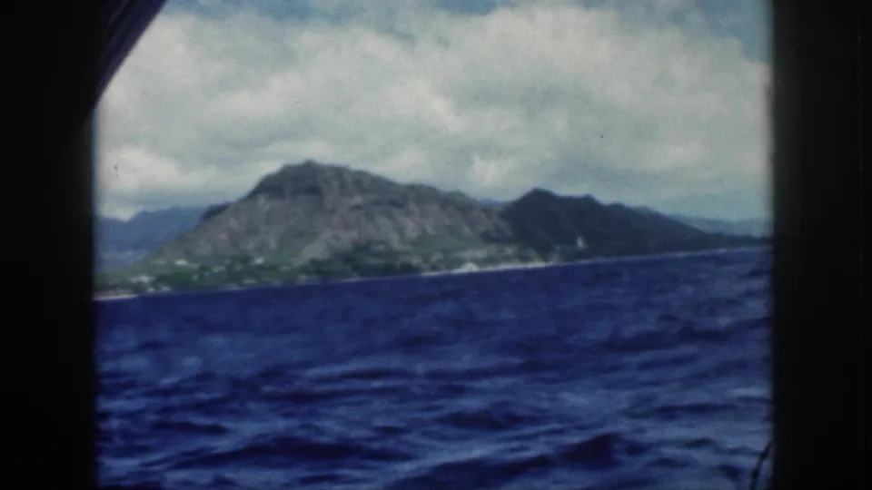Oahu's mountain coastline appears beyond dark boat-window framing in 1959 8mm home-movie footage from offshore.