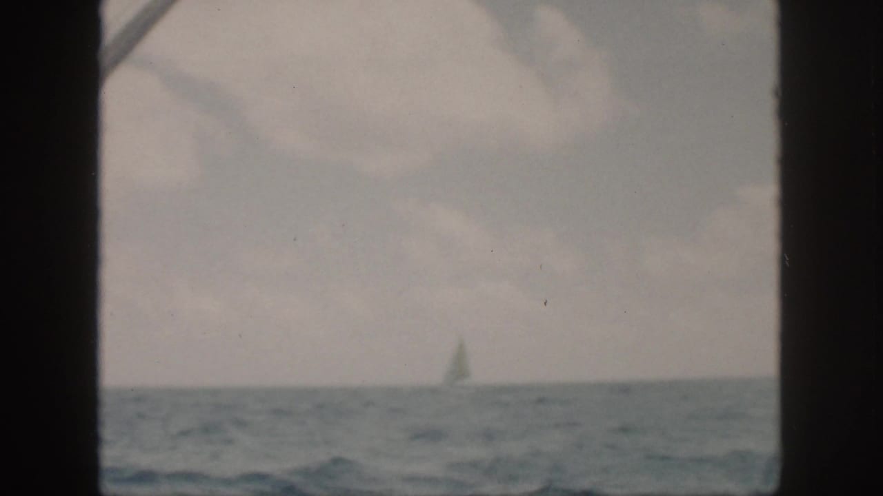 Distant sailboat on a pale horizon with ocean water and a dark boat frame.