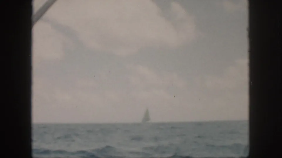 A distant sailboat appears on the horizon off Oahu, framed by the boat interior and muted 8mm color.