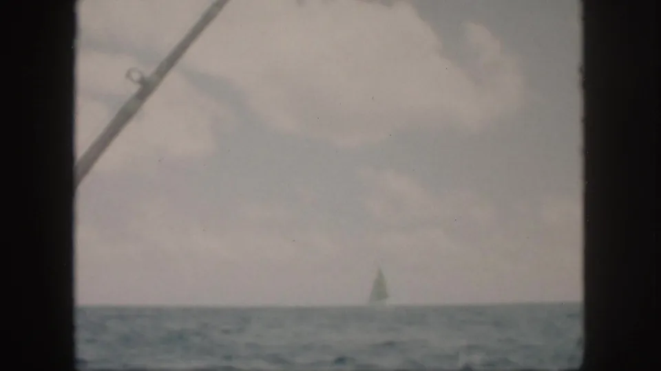 A distant sailboat remains on the Oahu horizon, seen through dark boat framing with faded 8mm color and soft focus.