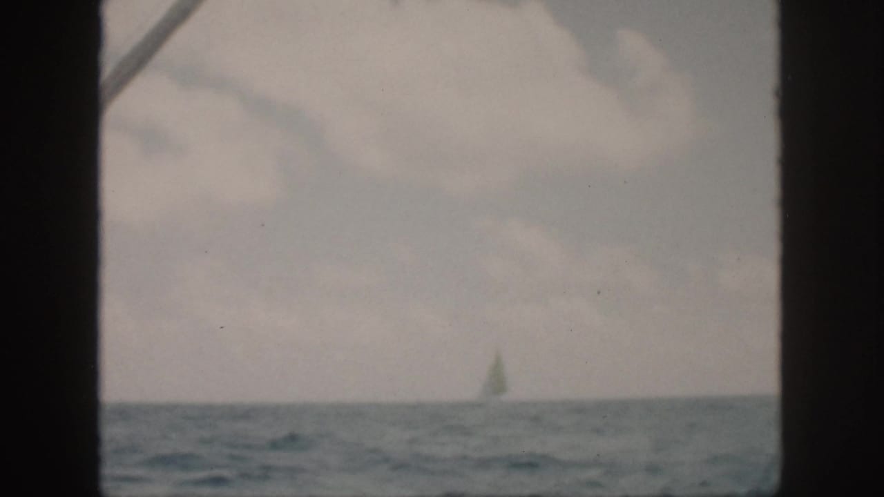 1959 Oahu 8mm frame showing a distant sailboat on open water, partly obscured by dark frame edges and soft exposure.