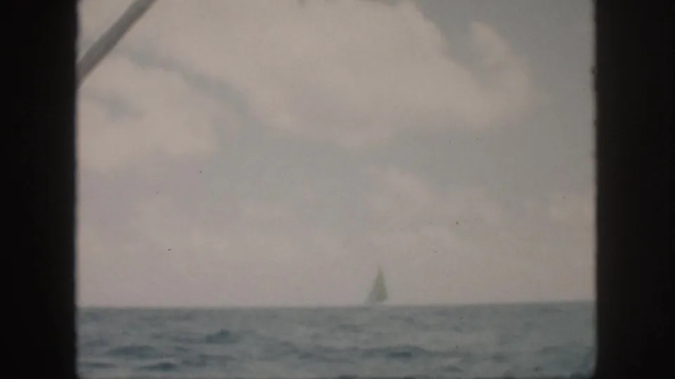 1959 Oahu 8mm frame showing a distant sailboat on open water, partly obscured by dark frame edges and soft exposure.