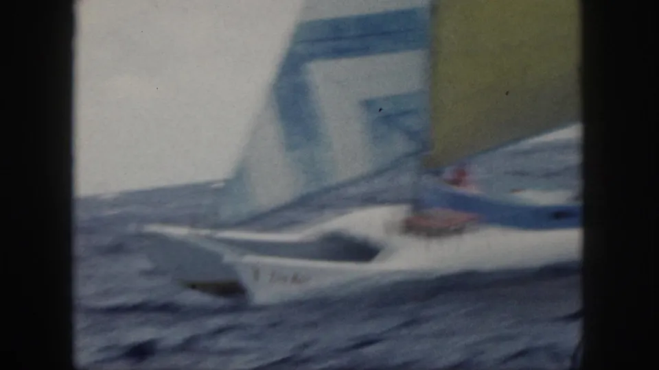 Soft 1959 Oahu 8mm frame with a partial view of a white catamaran, blue rigging, yellow sail, and ocean swell.