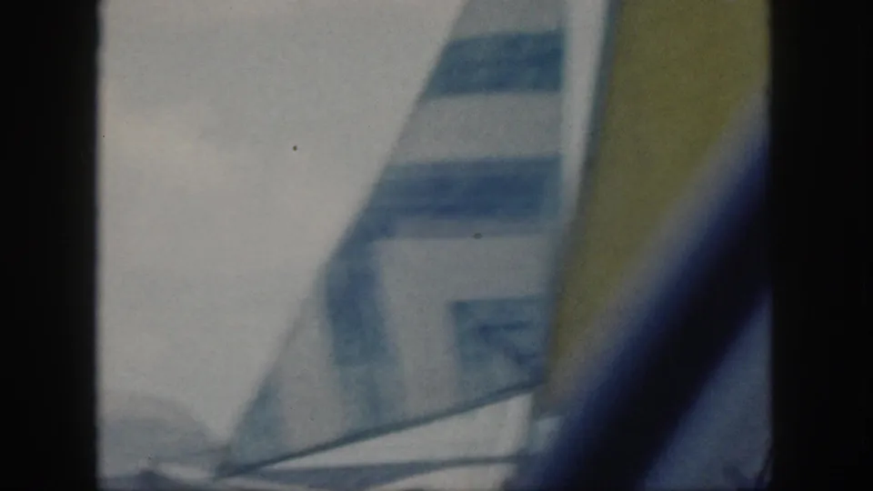 Soft 1959 Oahu 8mm frame with a striped sail and yellow sail edge crossing the view above ocean water.