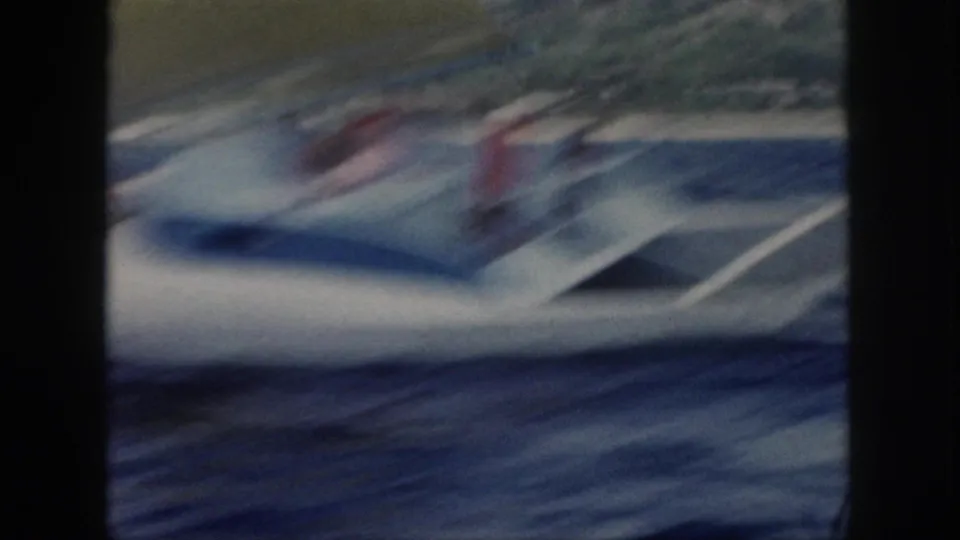 Motion-blurred 1959 Oahu 8mm frame showing the sailboat hull and a red-shirted person as the vessel cuts through waves.