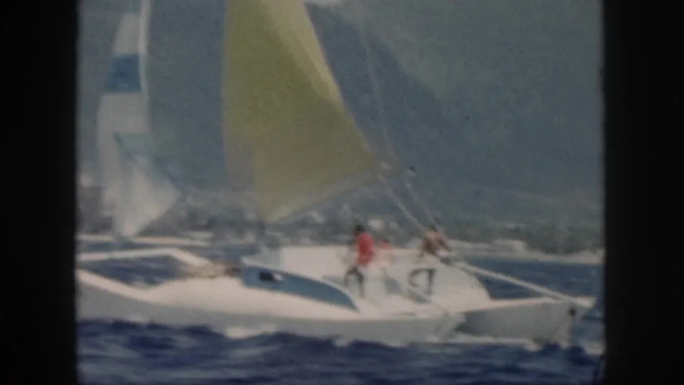 1959 Oahu home-movie frame of people standing on a white catamaran as it moves along the coast.