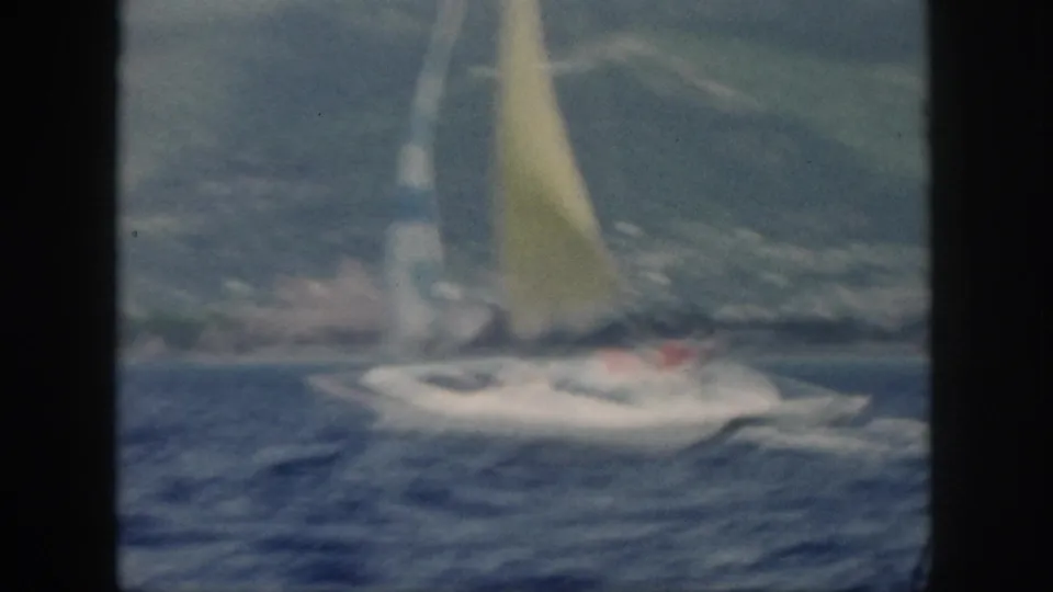 Soft 8mm frame from Oahu in 1959 showing a white catamaran moving across blue water with mountains and shoreline behind it.