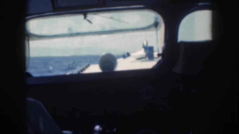 Onboard 1959 Oahu home-movie view through a boat window toward blue water, with part of another vessel or bow visible ahead.