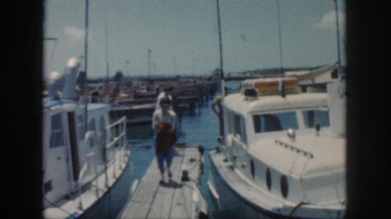 People on a narrow dock between white boats at a sunny marina.