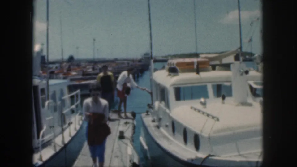 1959 Oahu marina frame showing people on a dock beside a white cabin boat and moored vessels.