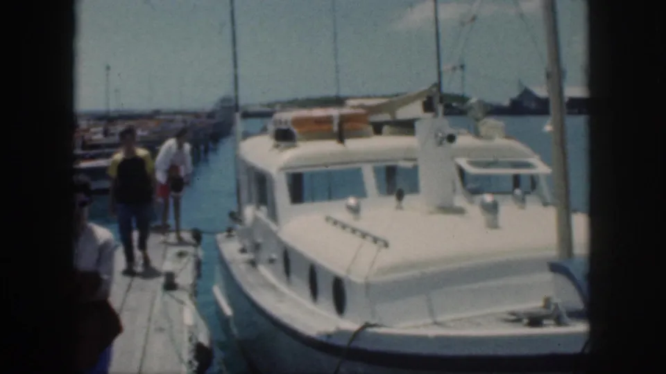 1959 Oahu home-movie frame with people walking away on a dock beside a white motorboat at the marina.