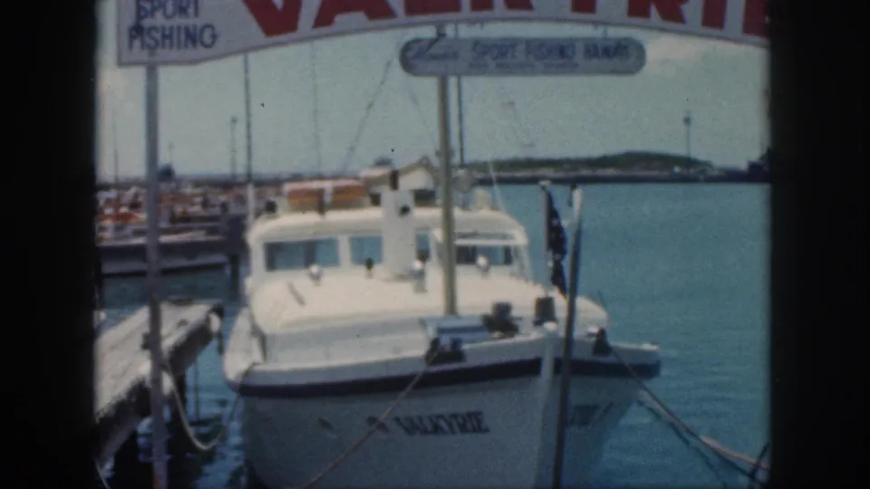 1959 Oahu home-movie view of Valkyrie moored at a dock, framed by marina signage, ropes, boats, and blue water.