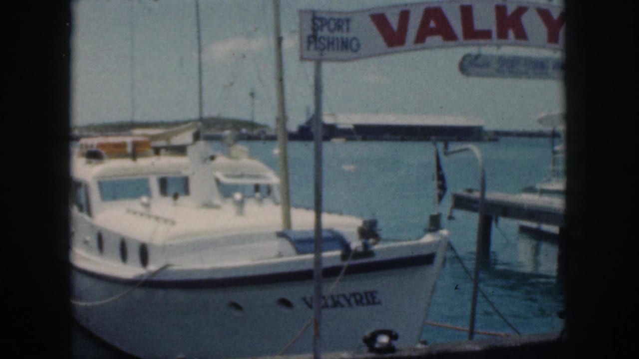 1959 Oahu home-movie frame of the white cabin cruiser VALKYRIE moored near a sport-fishing sign at a harbor.