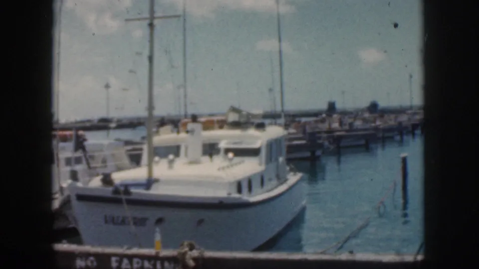 1959 Oahu harbor view showing the VALKYRIE cabin cruiser tied at dock with marina structures and masts in the background.