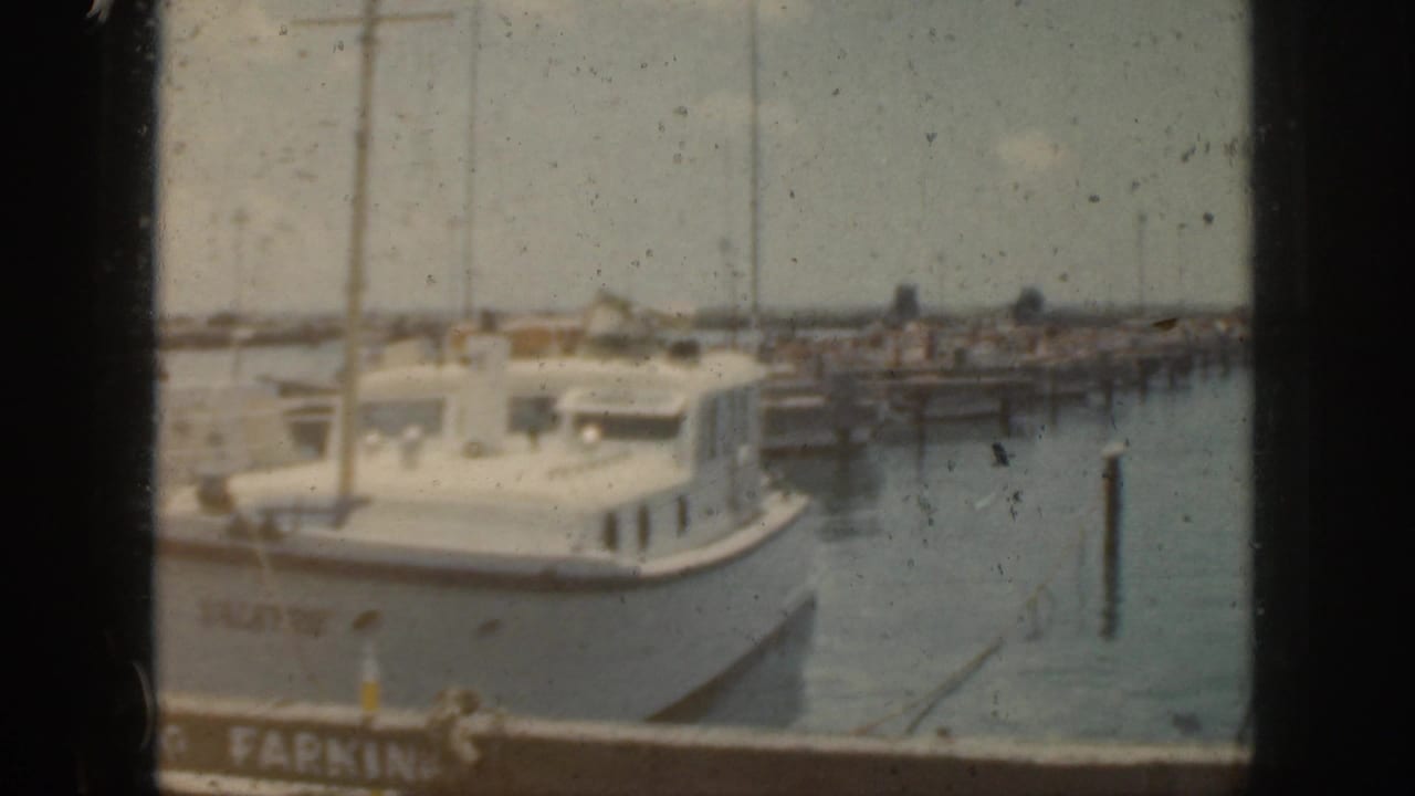 Faded 1959 Oahu harbor frame showing the docked VALKYRIE cabin cruiser, marina pilings, masts, and aged 8mm texture.