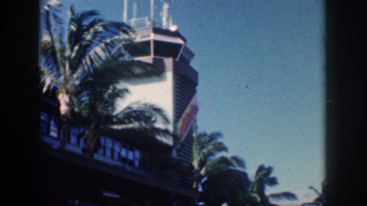 1959 Oahu airport exterior with palm trees crossing the control tower and soft, grainy 8mm color texture.