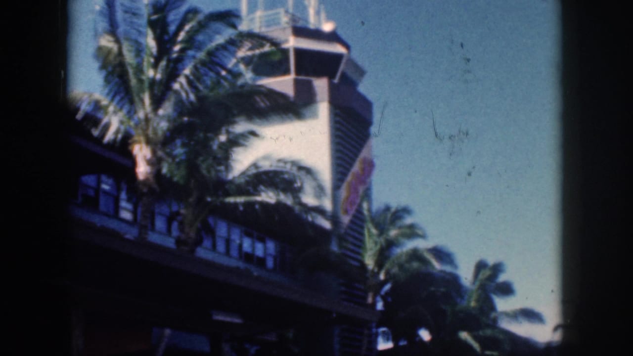 Oahu airport tower and palms at the end of the 1959 clip, with handheld framing, gate shadows, and faded 8mm color.