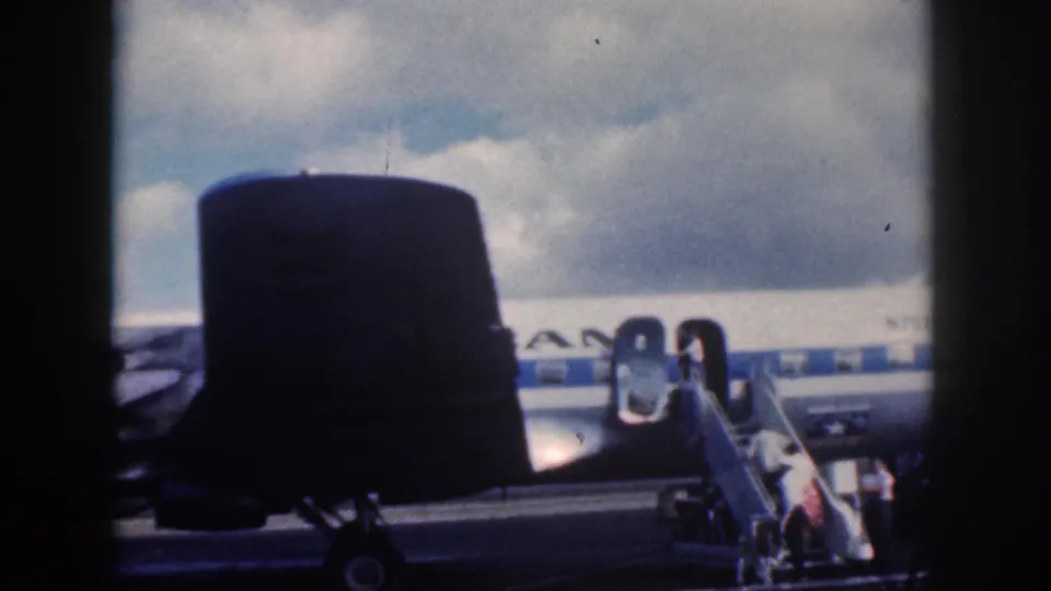 1959 Oahu airport view from another aircraft, with the tail and doorway of an American Airlines plane visible as passengers board.
