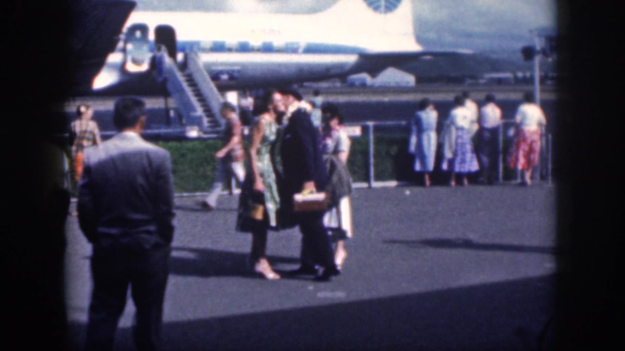 1959 Oahu airport arrival scene with passengers in suits and dresses standing near an airplane and stairs.
