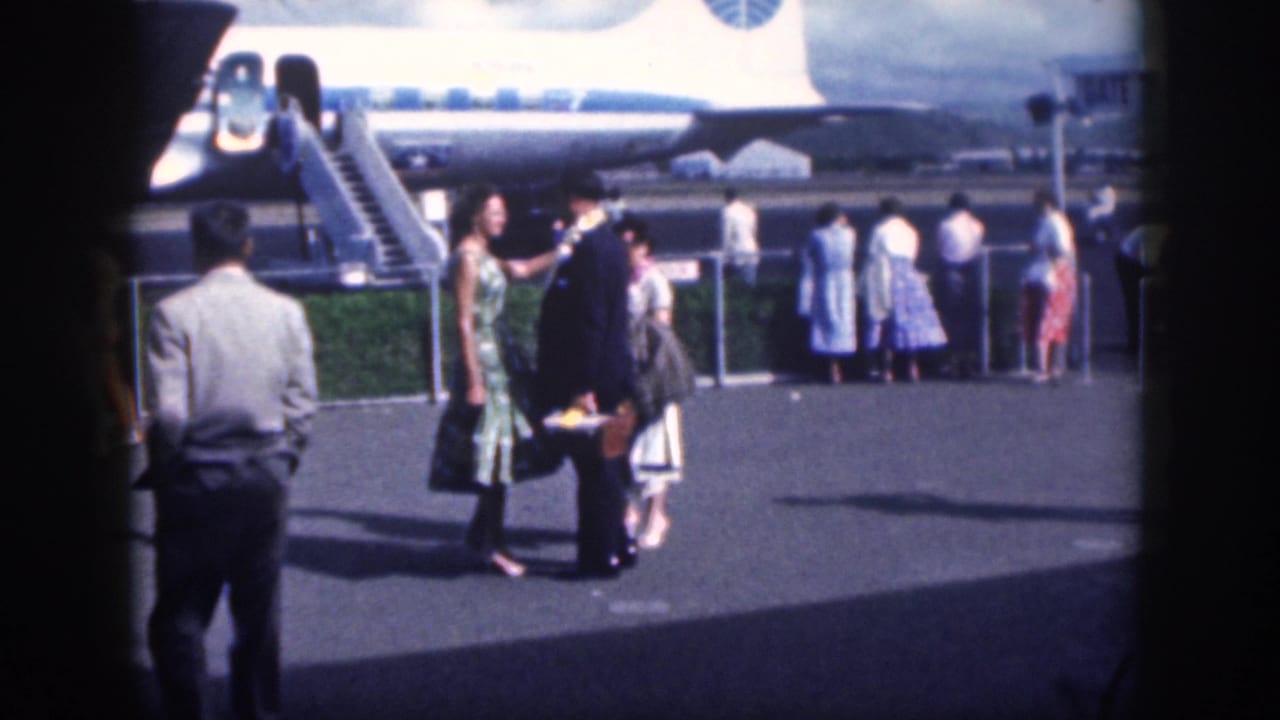 At a Honolulu airport in 1959, a uniformed man appears to greet a woman as passengers stand by the aircraft.