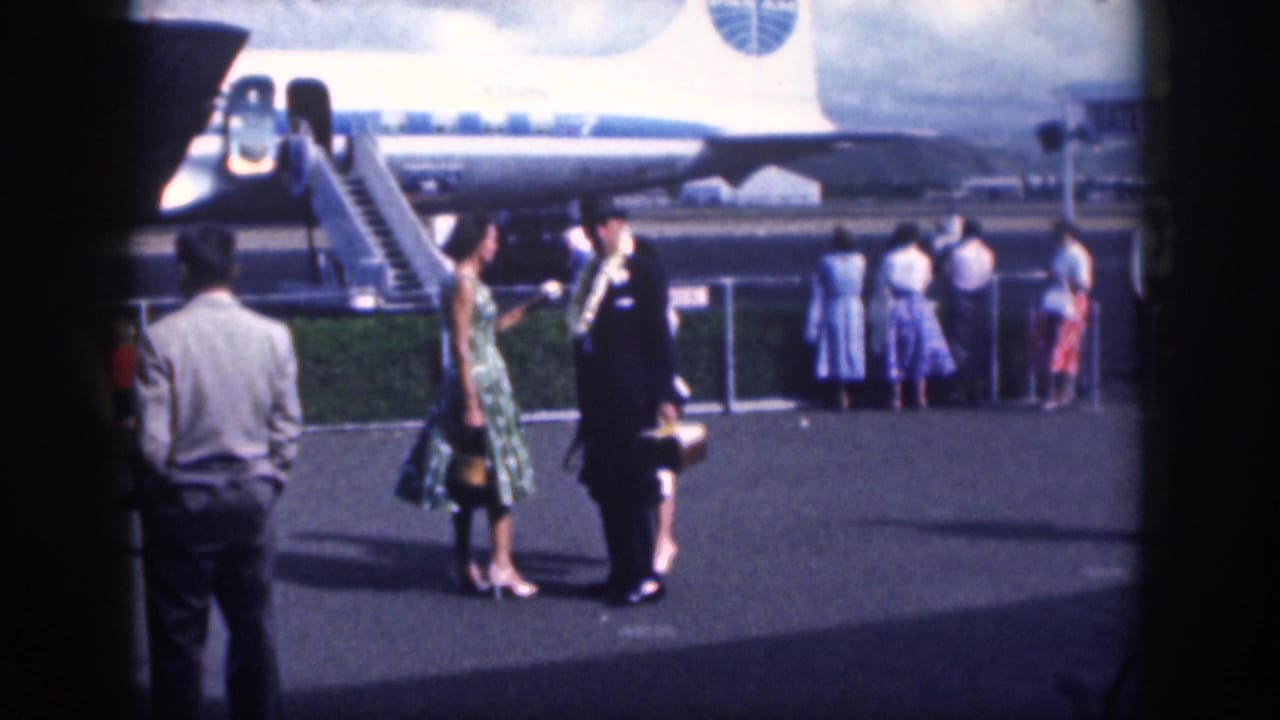 Home-movie view of 1959 Oahu airport passengers and a uniformed greeter beside a commercial aircraft.
