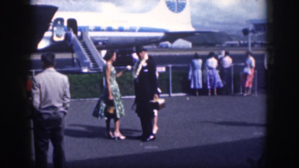 Home-movie view of 1959 Oahu airport passengers and a uniformed greeter beside a commercial aircraft.