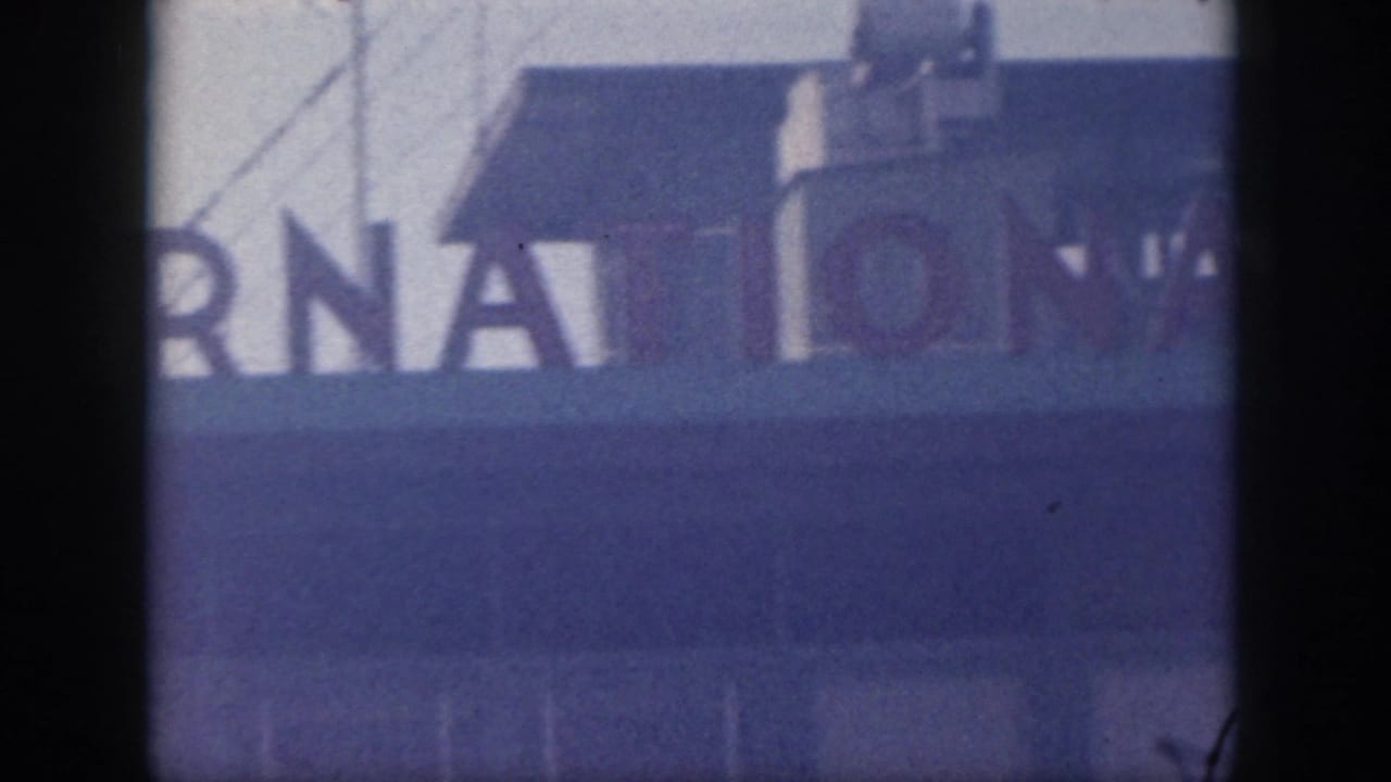1959 Oahu airport signage appears in close crop, with partial large letters on a pale blue facade and dark vertical obstructions.