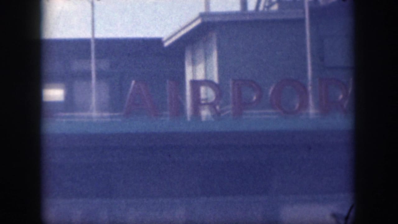 The pan reveals more of the airport sign, including bold letters from the word airport on a light blue exterior wall.