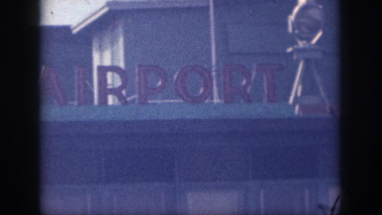 Final close frame of the airport sign shows cropped airport lettering, a blue facade, and a metal structure at the right edge.