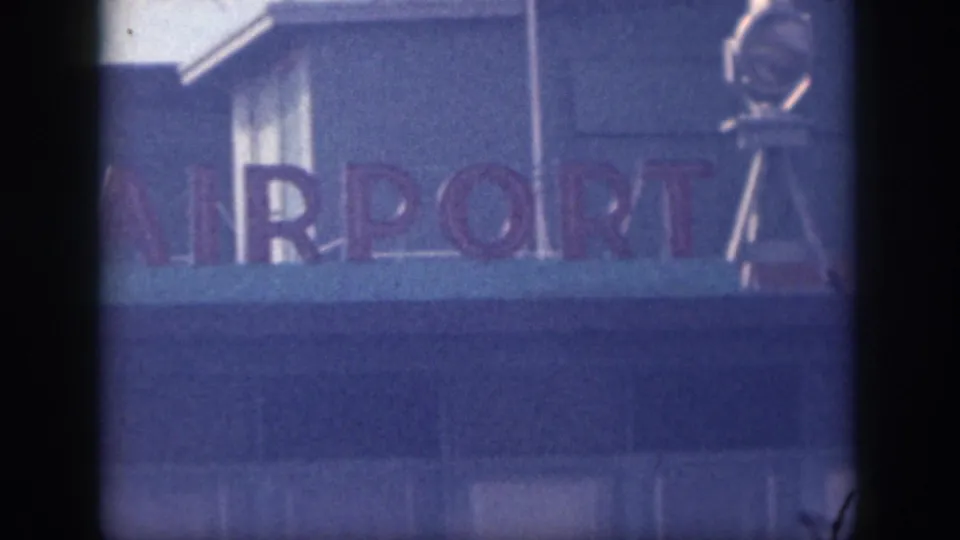 Final close frame of the airport sign shows cropped airport lettering, a blue facade, and a metal structure at the right edge.