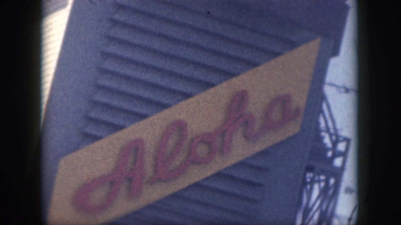 Diagonal Aloha sign in pink script against a blue corrugated wall.