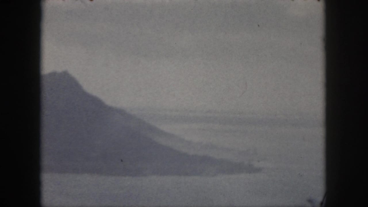 1959 Oahu 8mm frame showing a distant hazy mountain across calm coastal water with soft sky above.