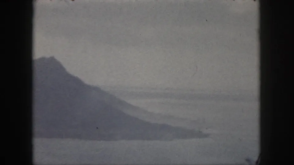 1959 Oahu 8mm frame showing a distant hazy mountain across calm coastal water with soft sky above.