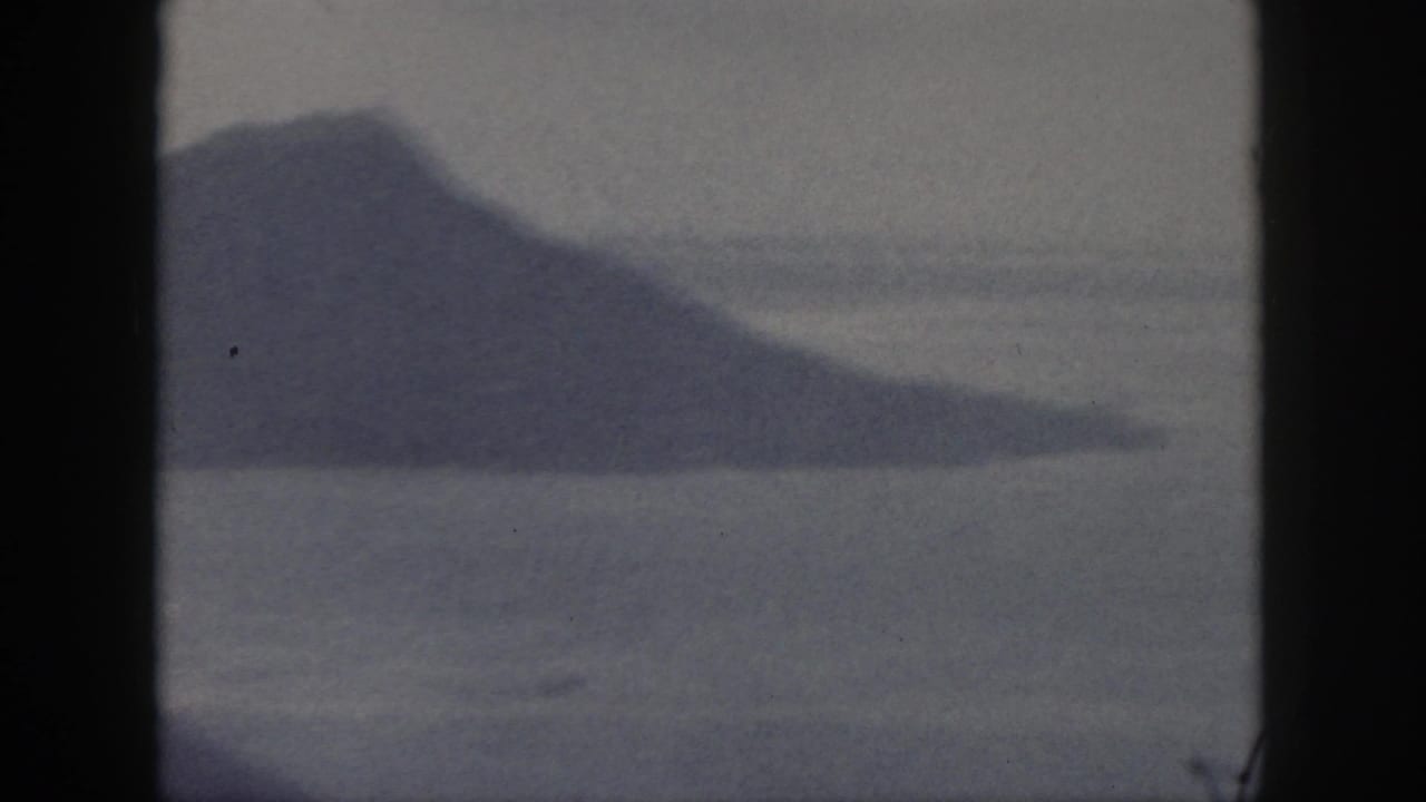 Distant mountain and shoreline seen across water through soft film grain.