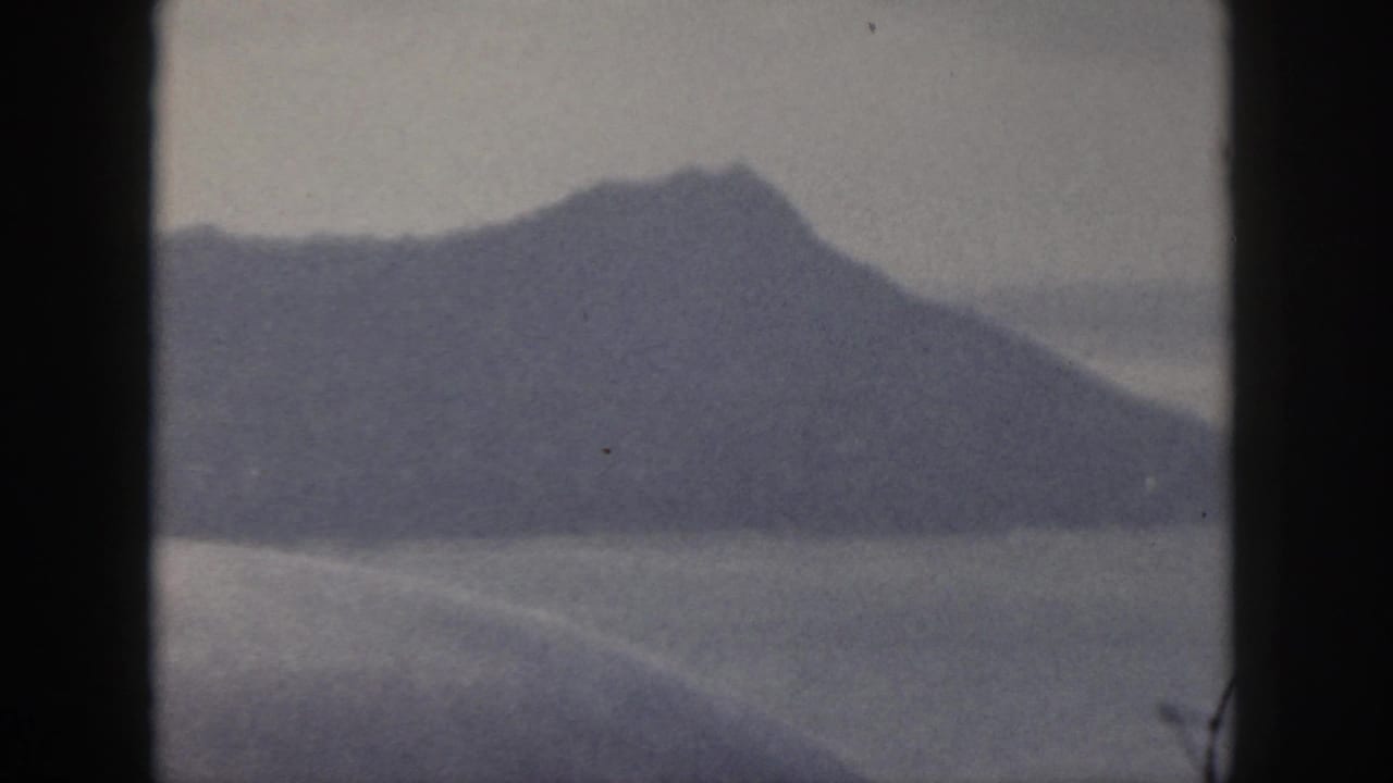 1959 Oahu 8mm frame showing a dark island mountain silhouette across water with muted blue-gray tones.