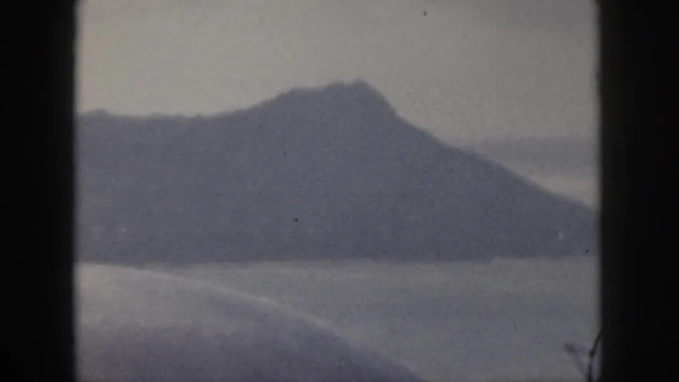 1959 Oahu 8mm frame showing a dark island mountain silhouette across water with muted blue-gray tones.
