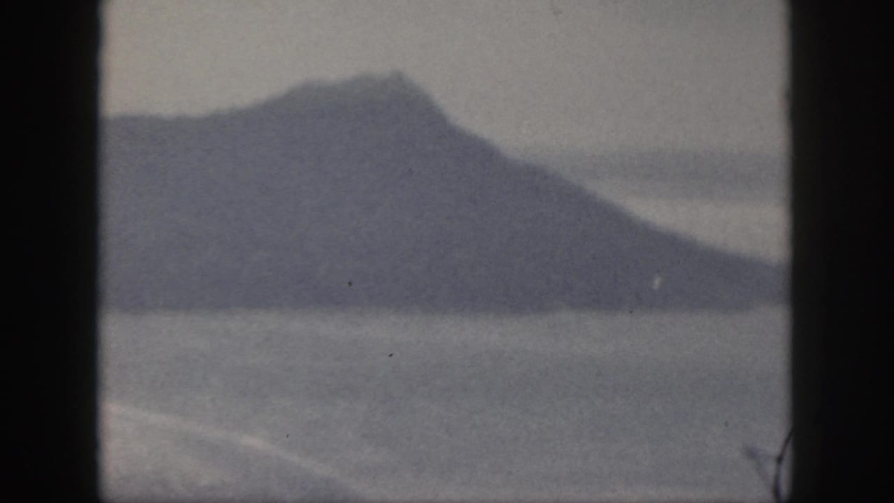 1959 Oahu 8mm frame showing a hazy mountain or grassy hill across water, bordered by dark vertical edges.
