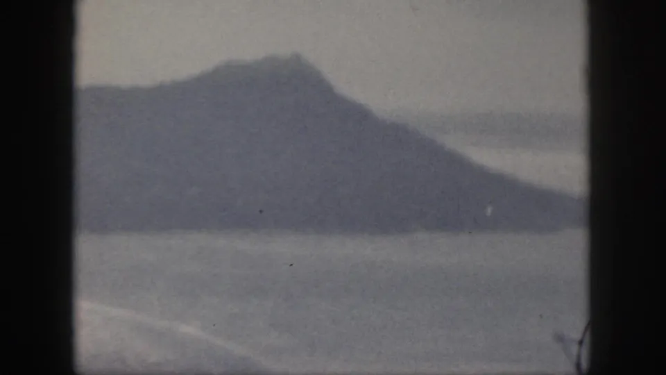 1959 Oahu 8mm frame showing a hazy mountain or grassy hill across water, bordered by dark vertical edges.
