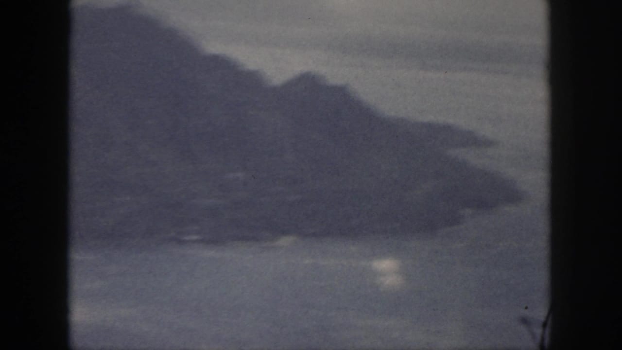 1959 Oahu 8mm frame showing a soft, grainy shoreline and mountain slope across water.
