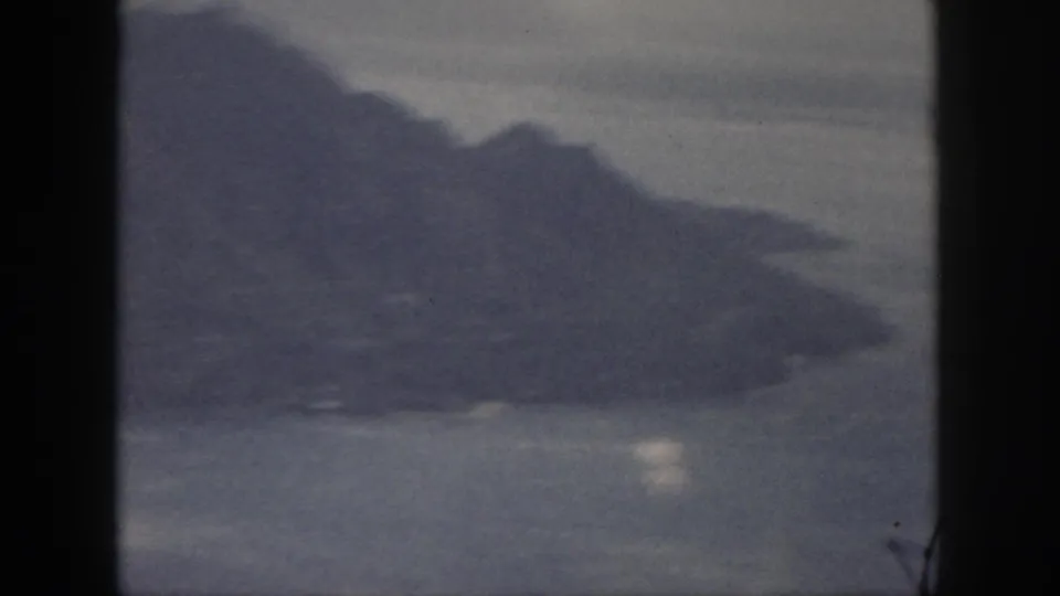 1959 Oahu 8mm frame showing a soft, grainy shoreline and mountain slope across water.