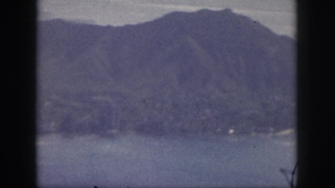 Aerial coastline view with mountains, water, haze, and vertical film border.